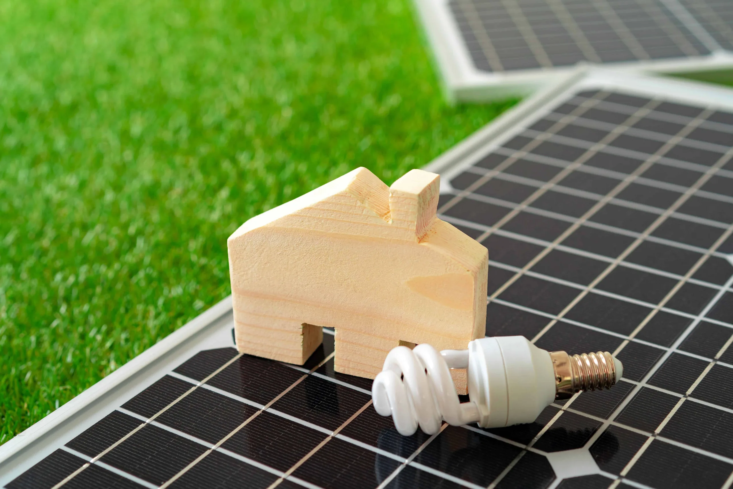 Holzhausmodell und Energiesparlampe auf Solarpanel.